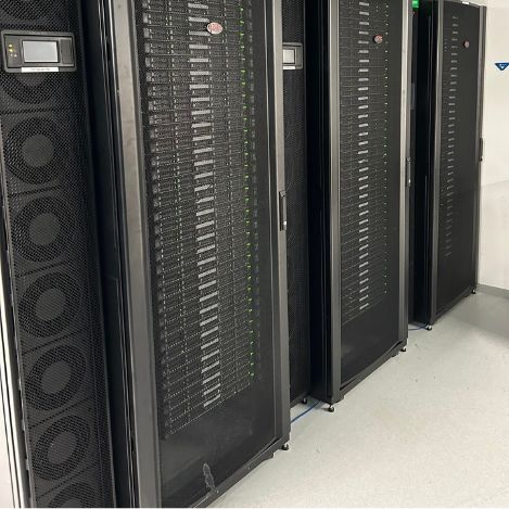 Rows of black server cabinets in a data center room, with visible cables and equipment behind mesh doors on a bright floor, demonstrate Tal Systems' expertise in building server farms and advanced server farm solutions for companies.